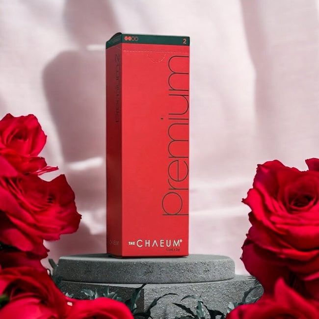 CHAEUM PREMIUM NO2 dermal filler packaging in red box surrounded by red roses on a grey stone pedestal